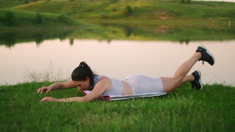 Woman-stretches-her-back-and-makes-bends-lying-on-the-grass-girl-trains-in-the-city-park-in-nature.